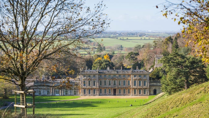A sweeping autumn view between trees down grassy parkland to the east front of the house at Dyrham Park